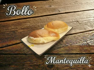 Dos bollos con mantequilla sobre un plato blanco, sobre una mesa de madera.