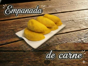 Cuatro empanadas de carne sobre un plato blanco, con fondo de mesa de madera.
