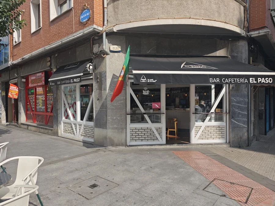 Bar cafetería "El Paso" en una esquina, con toldo negro y bandera de Italia.
