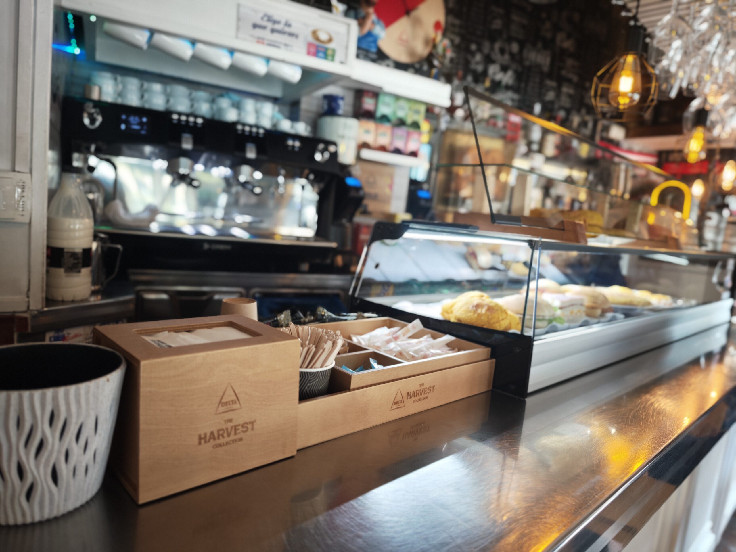 Mostrador de café con cajas de madera, utensilios y una vitrina de alimentos.