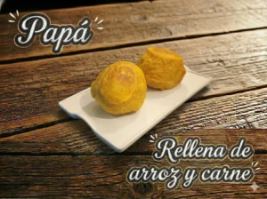 Dos papas rellenas de arroz y carne sobre un plato blanco, con fondo de madera.