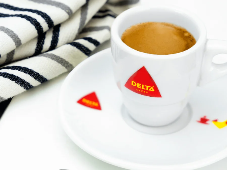 Taza de café expreso con plato blanco y logotipo de Delta, sobre una mesa.