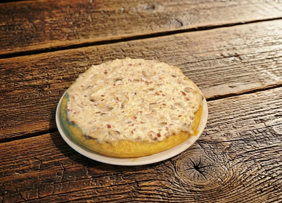 Tarta con una capa de crema y trozos de jamón sobre una base dorada.